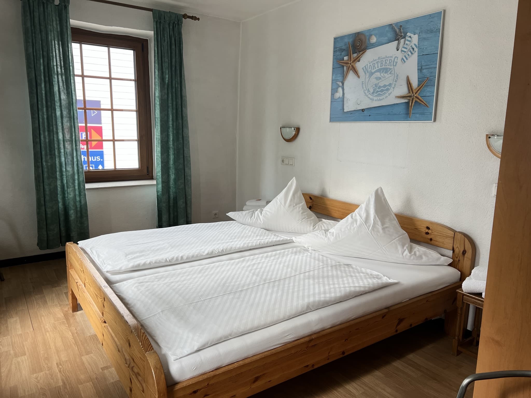 Apartment der Aal-Kate Wuppertal mit hellem Schlafzimmer, Doppelbett aus Holz, grünem Vorhang und maritimer Wanddekoration.